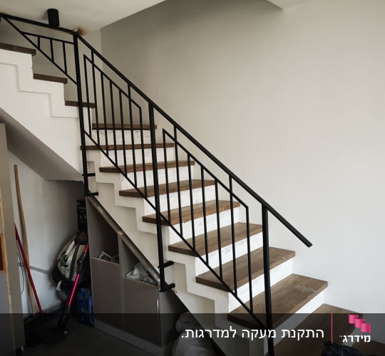 מעקה מתכת שחור על מדרגות עץ ולבן